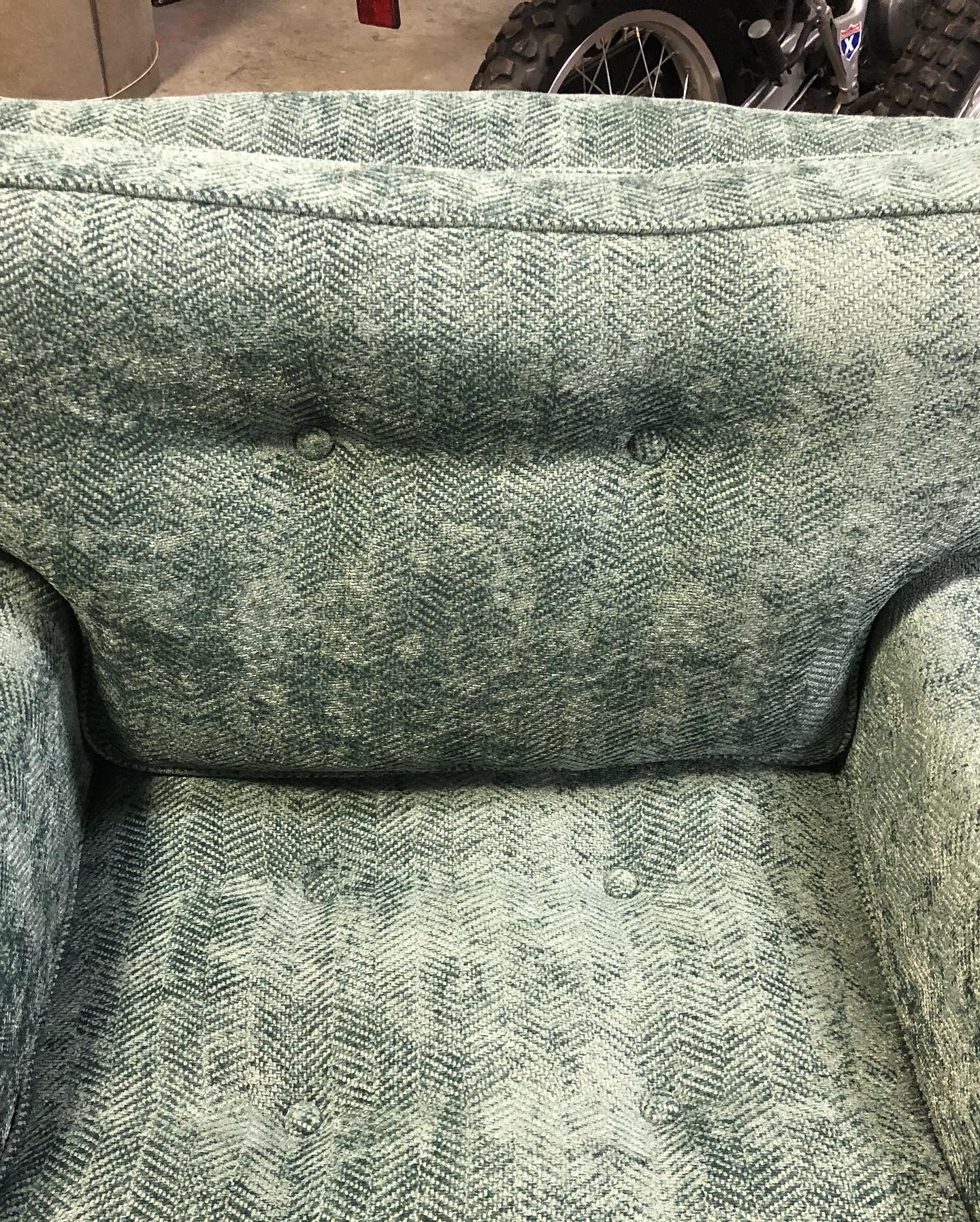 A close up of a green chair with a wheelchair in the background.