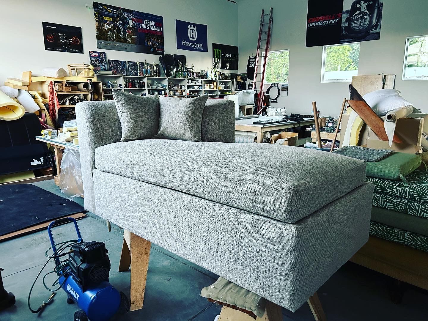 A grey couch is sitting in a room with a blue air compressor.