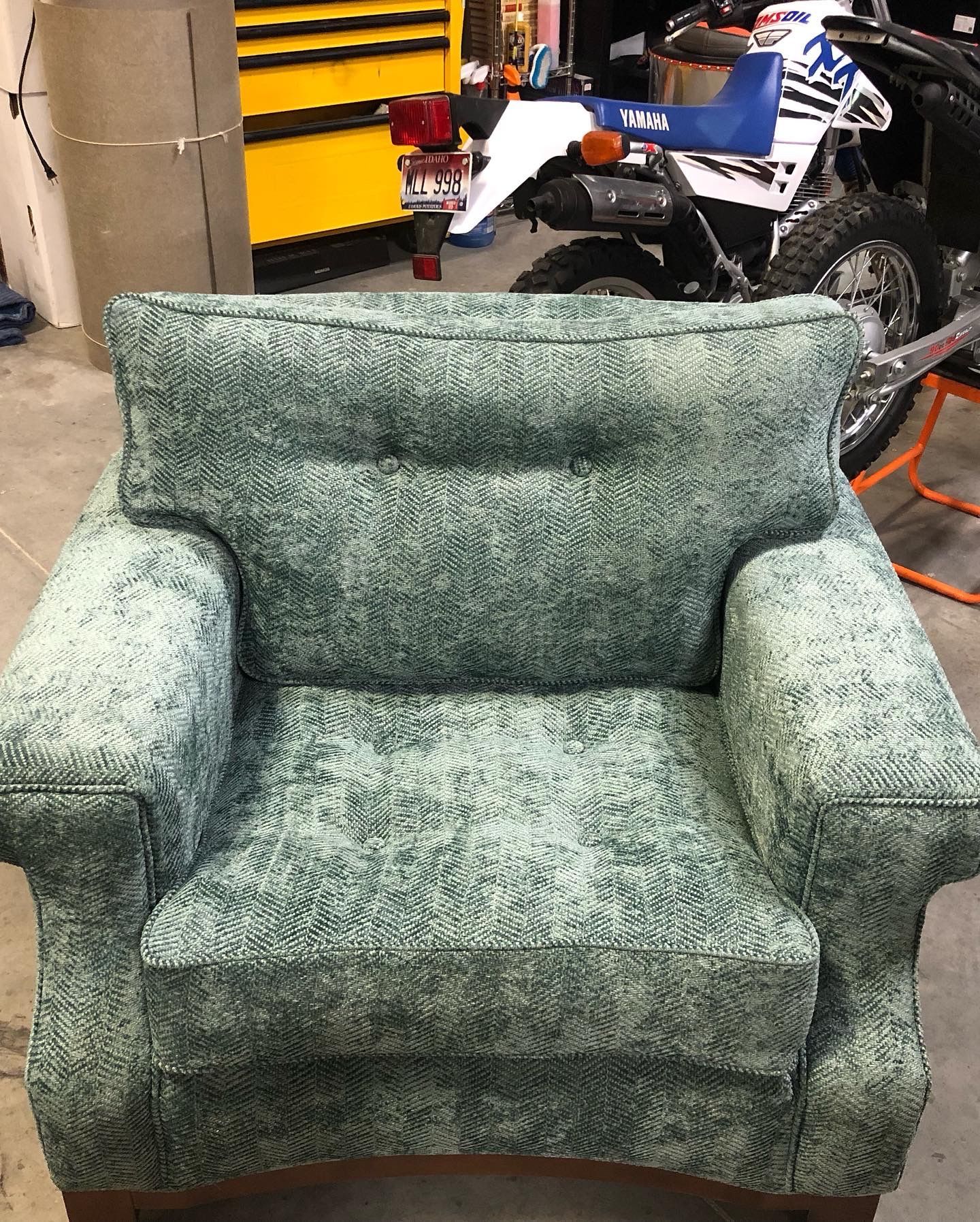 A green chair is sitting in front of a motorcycle in a garage.