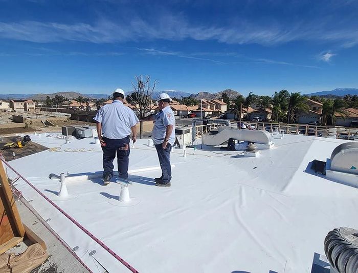 Two men are standing on top of a white roof.