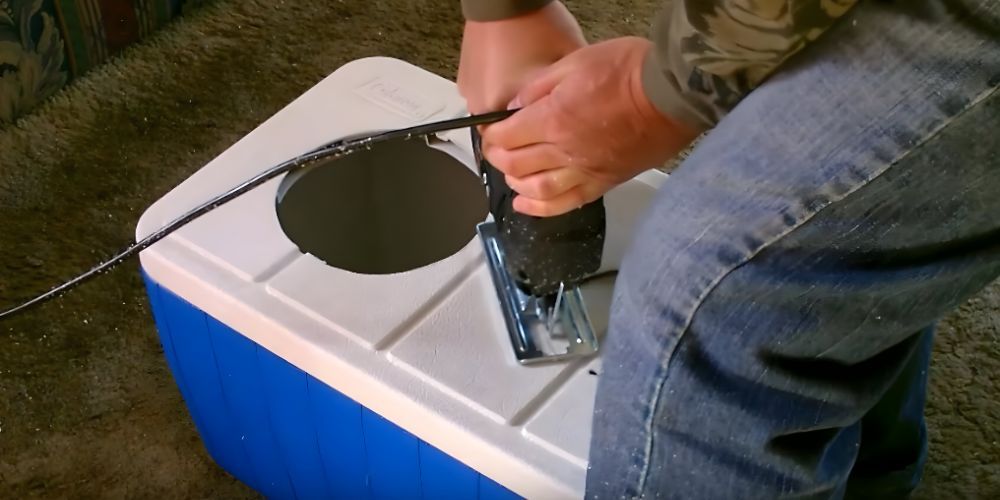 A person is cutting a hole in a cooler with a jigsaw.