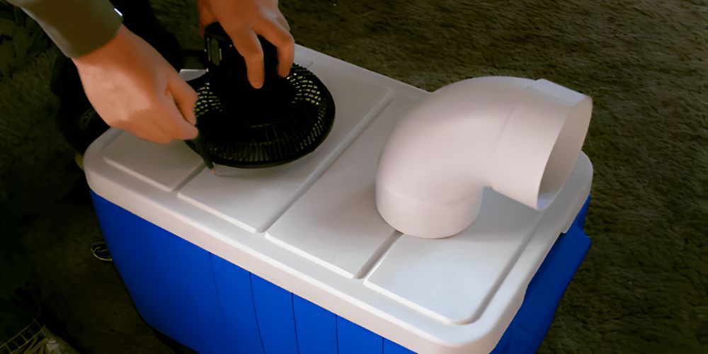 A person is holding a fan on top of a blue cooler.