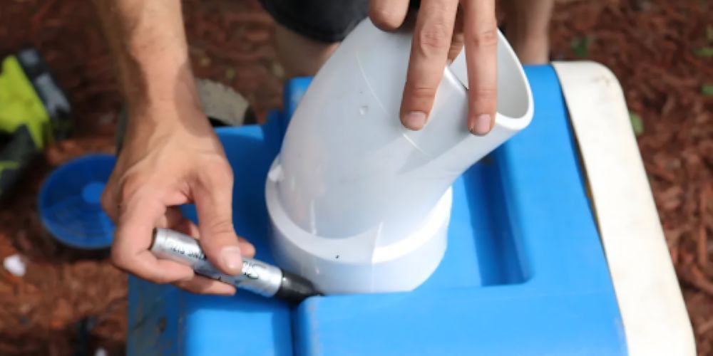 A person is using a drill to drill a hole in a blue cooler.