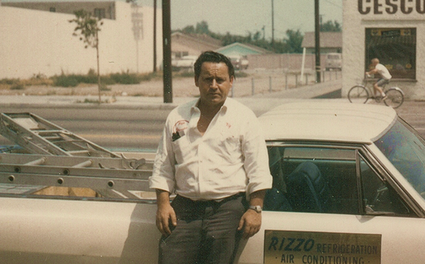 A man standing next to a car that says rizzo on the door