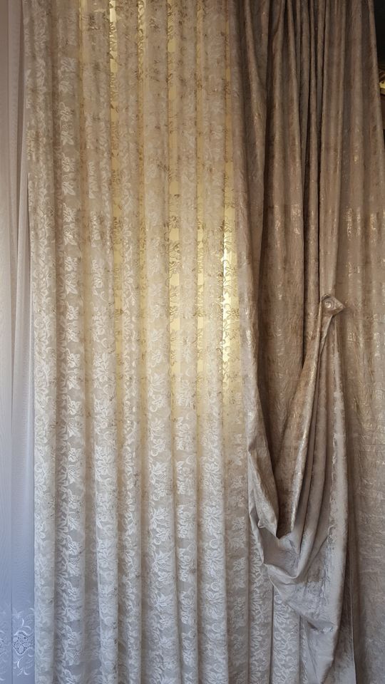 Tende plissettate beige con un fermatenda drappeggiato sulla destra, che coprono una finestra.