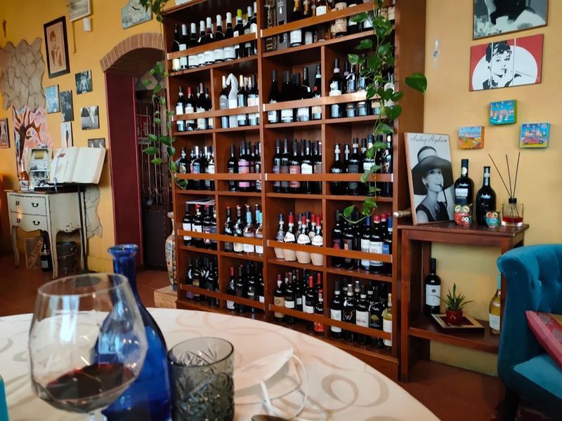 Una stanza accogliente con una grande rastrelliera in legno piena di bottiglie, un tavolo in primo piano con del vino e pareti gialle.