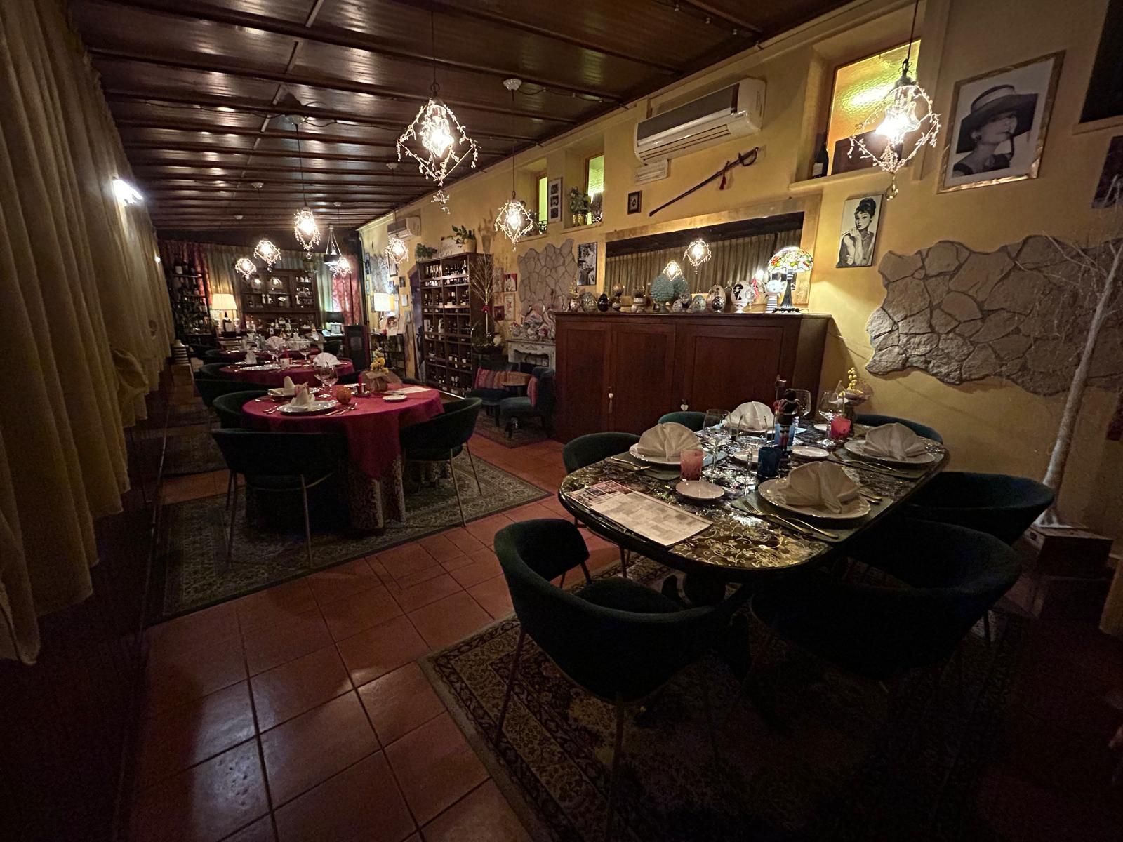 Una sala da pranzo interna con tavoli e sedie scure, luci soffuse e tappeti decorati su un pavimento piastrellato.