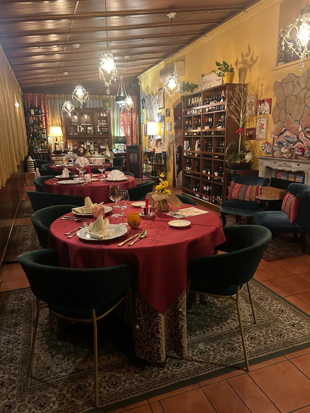 Un interno accogliente e illuminato da una luce calda, con tavoli ricoperti da tovaglie rosse, apparecchiati con cura e sedie in velluto scuro.
