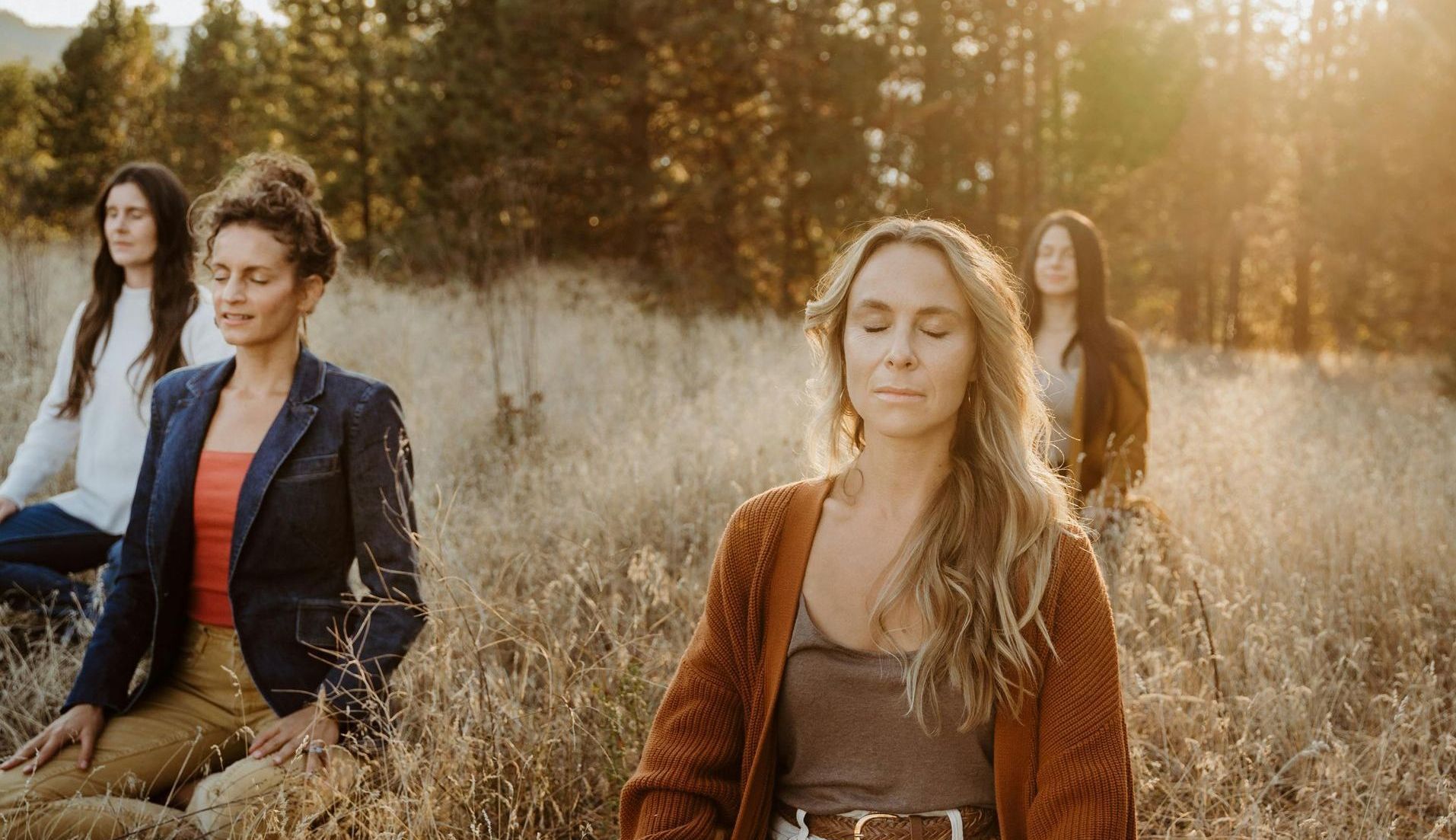 A group of women are sitting in a field with meditating.