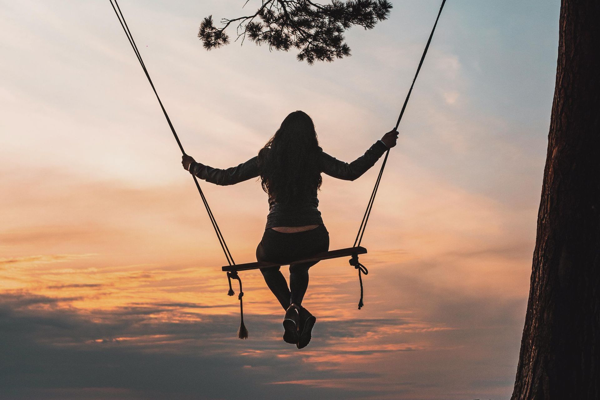 A woman is sitting on a swing at sunset