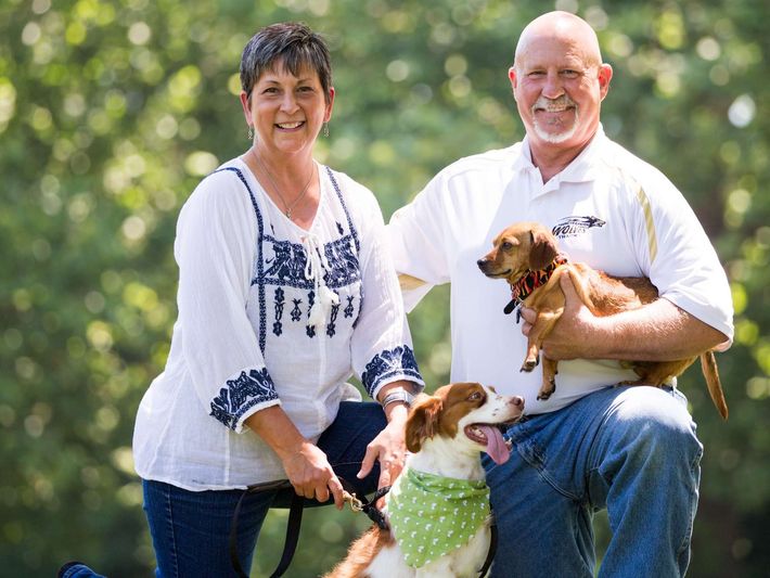 A man and a woman are posing for a picture with their dogs.