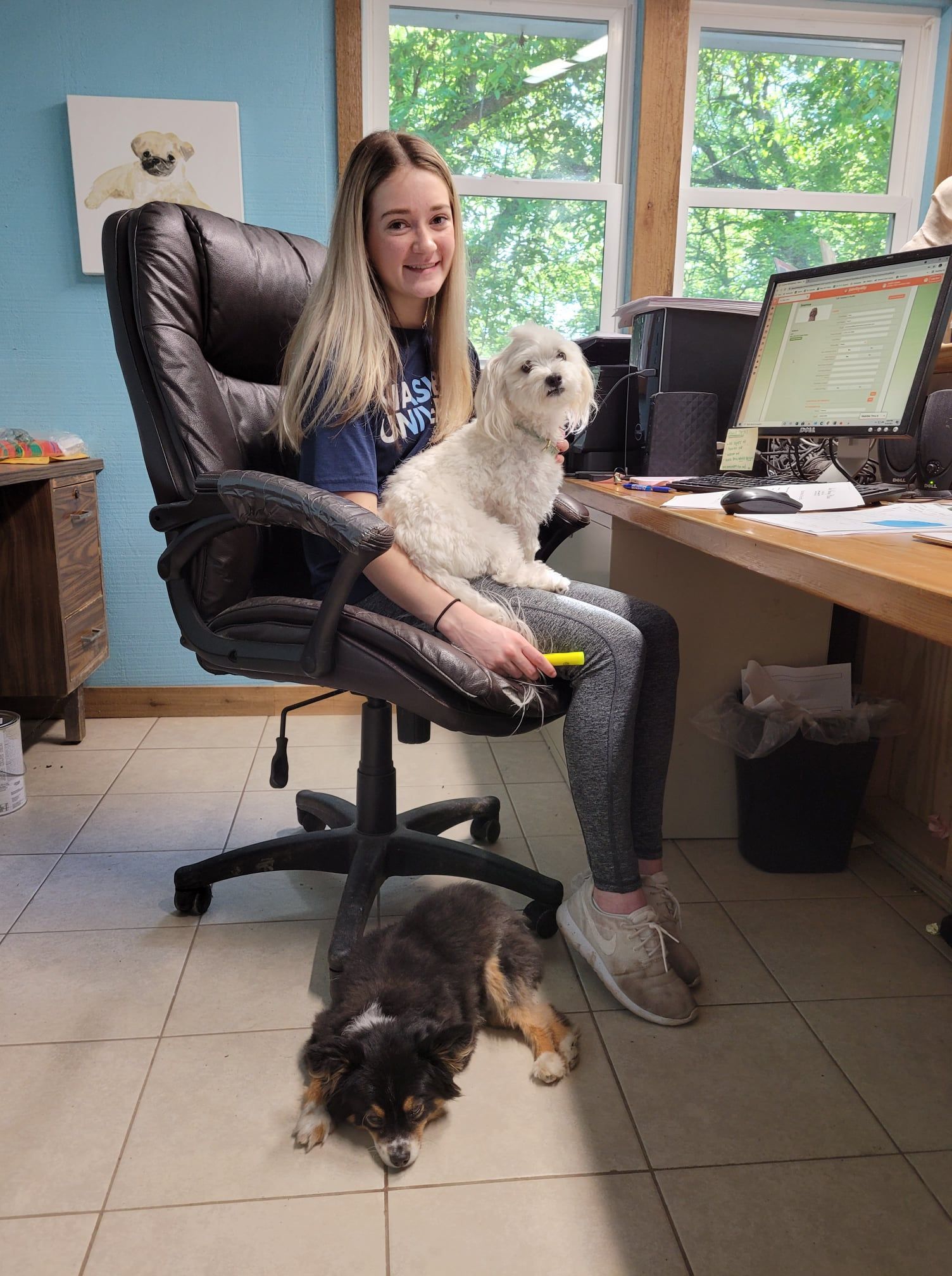 A woman is sitting in an office chair with a dog on her lap.