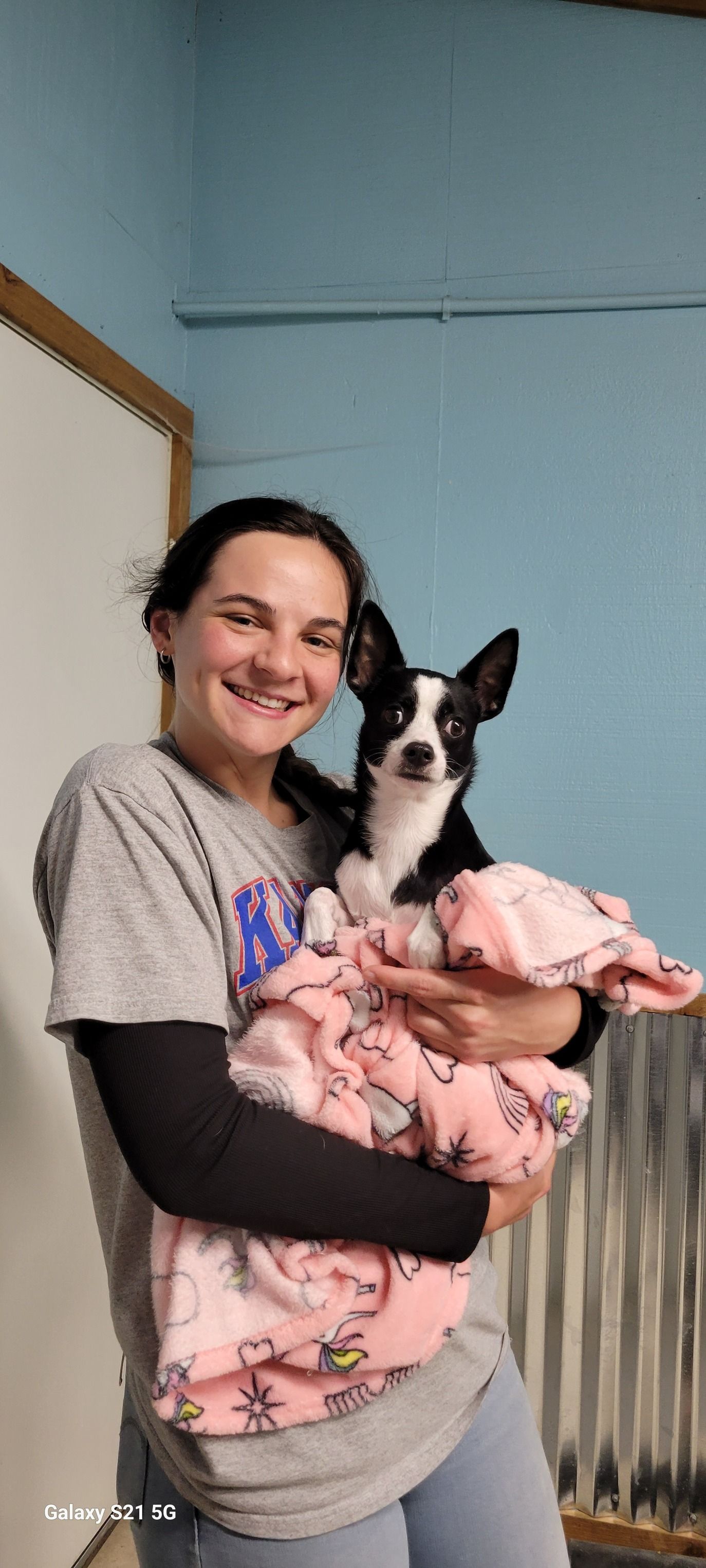 A woman is holding a black and white dog in her arms.