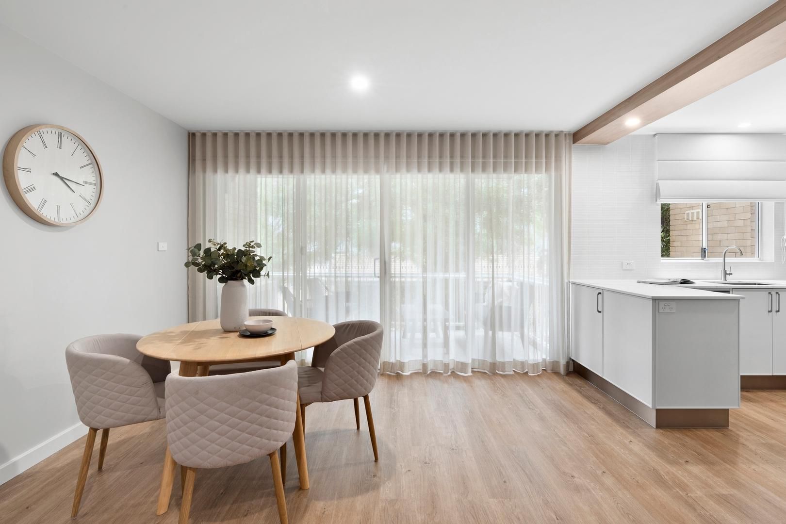 A dining room with a table and chairs and a clock on the wall.
