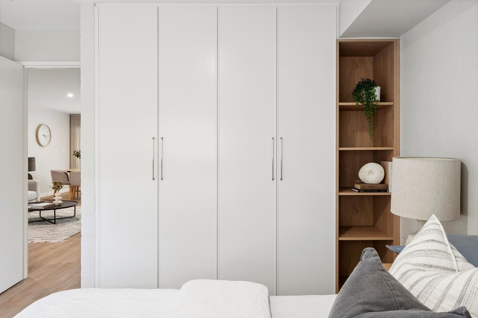 A bedroom with a bed , wardrobes , shelves and a lamp.