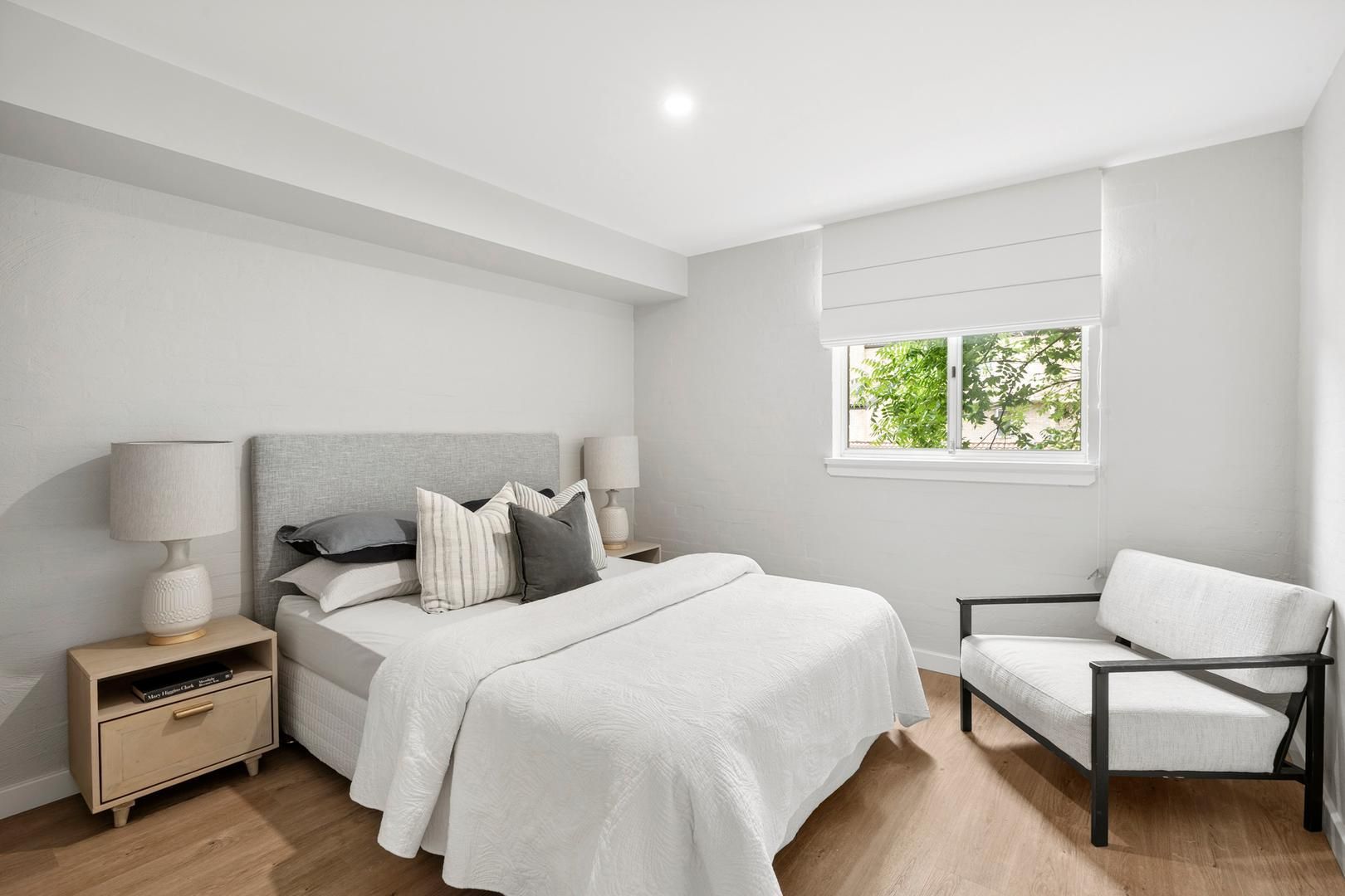 A bedroom with a bed , chair , nightstand and window.