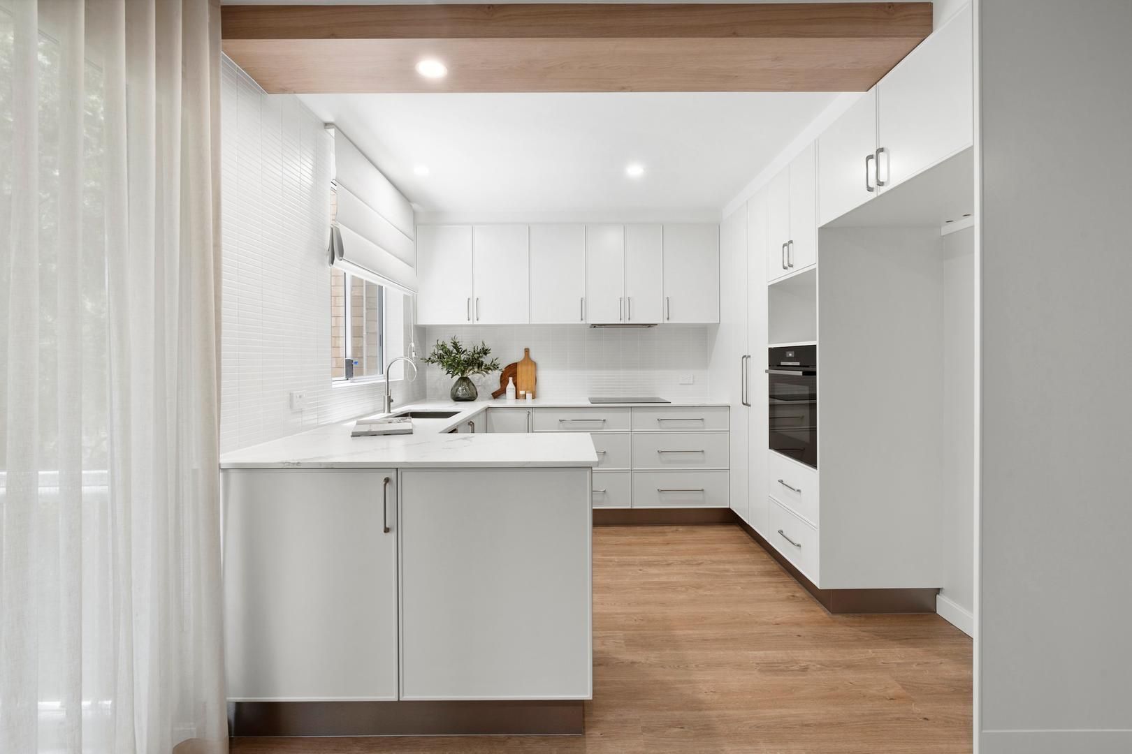 A kitchen with white cabinets and wooden floors.
