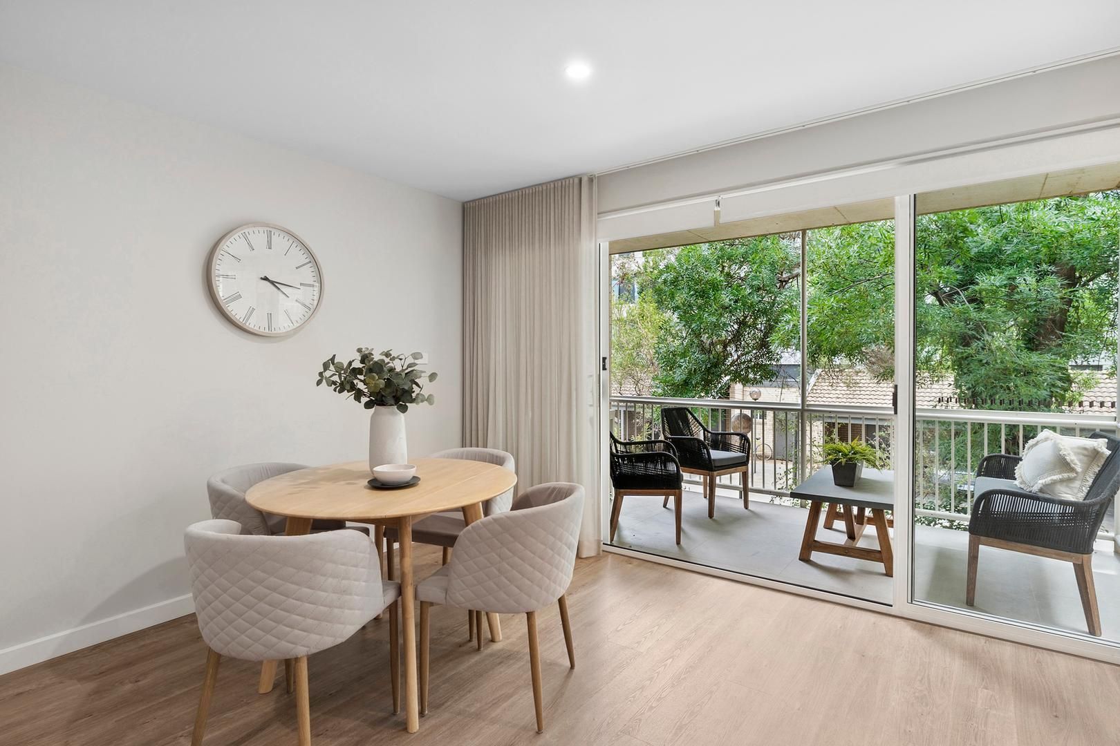 A living room with a table and chairs and a clock on the wall.