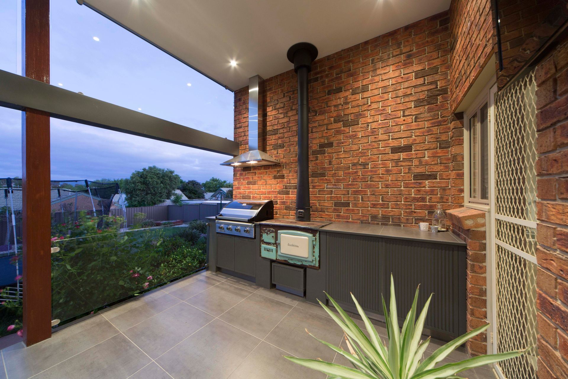 Outdoor kitchen with brick wall, grill, and view of yard.