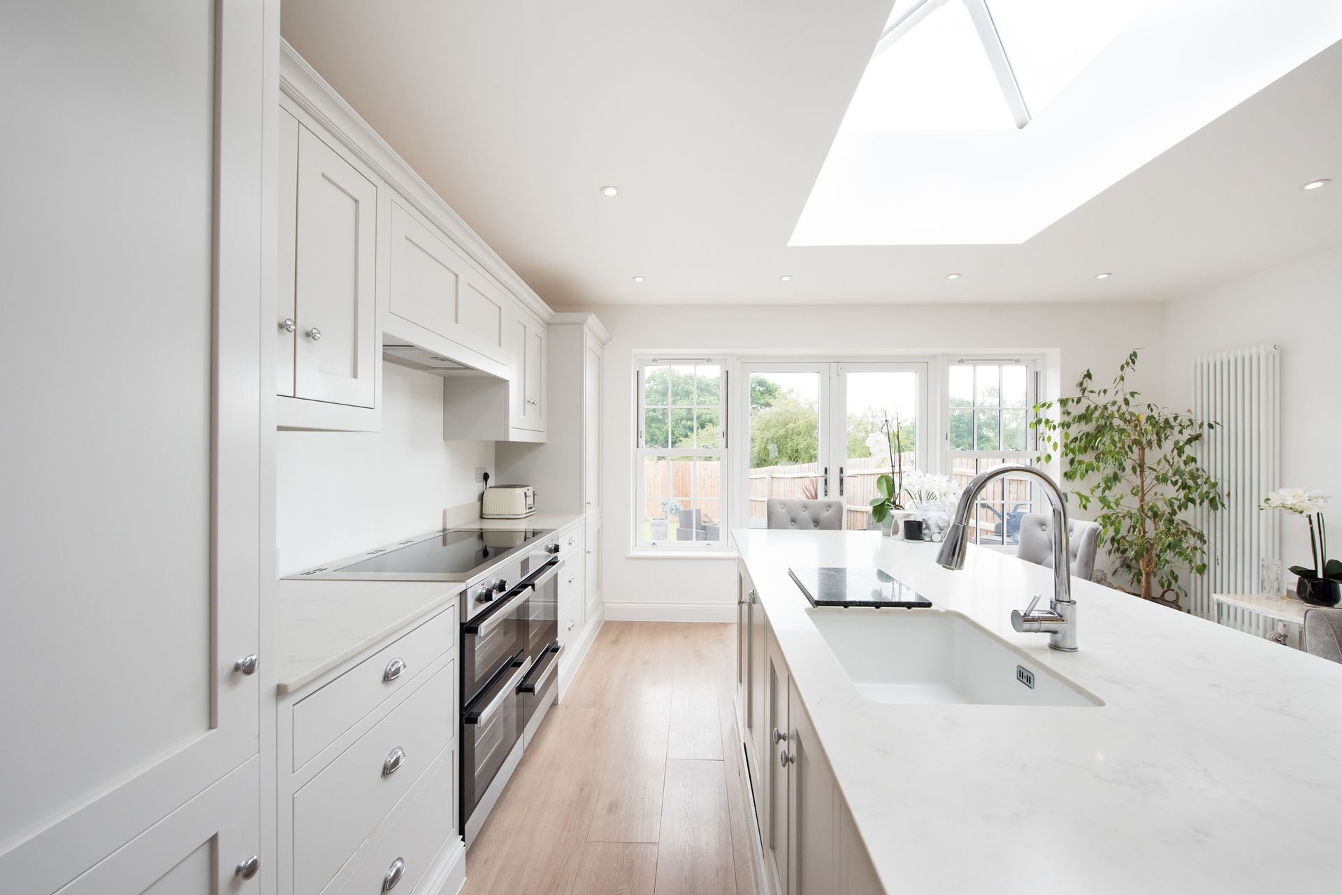 A kitchen with white cabinets , a sink , a stove , and a skylight.