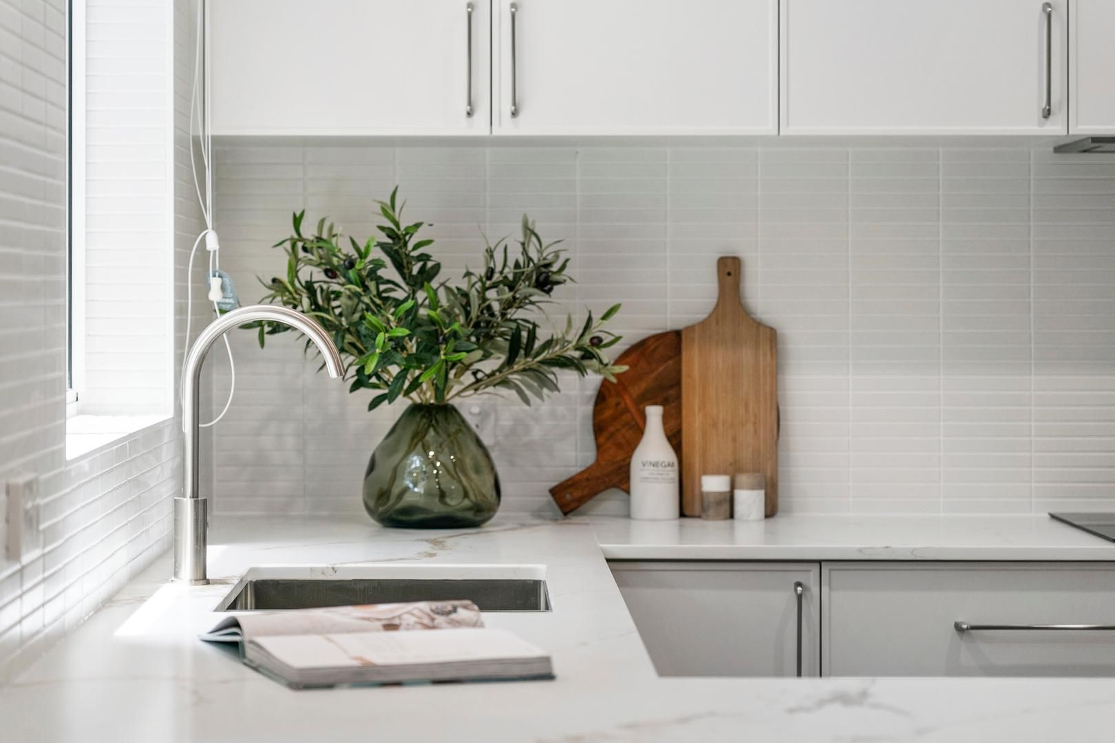 A kitchen with white cabinets and a sink with a vase of flowers on the counter.