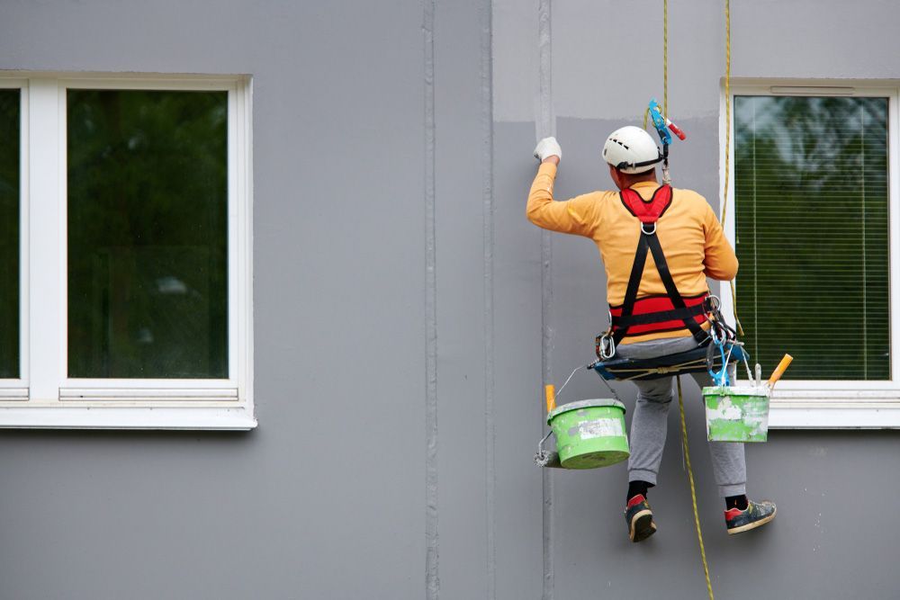 Worker Hanging On Rope And Paints Building Walls — Professional Painters in Ballina, NSW