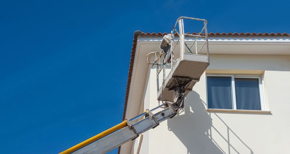 A Man Paints The Side Of A Building On A Crane — Professional Painters in Casuarina, NT