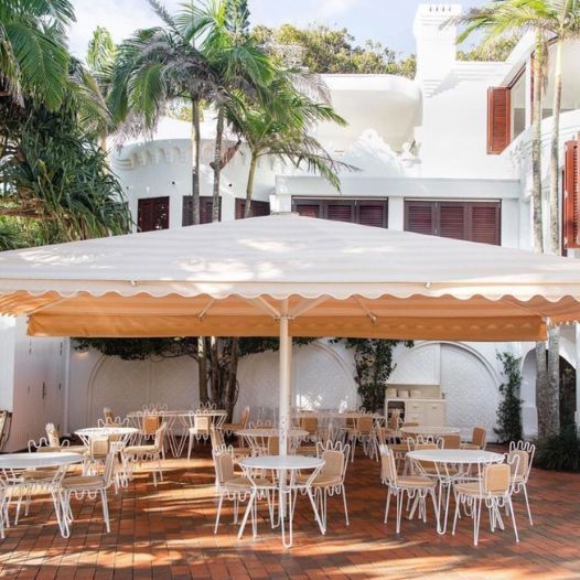 Tables And Chairs Under An Umbrella In Front Of A White Building — Professional Painters in Suffolk Park, NSW