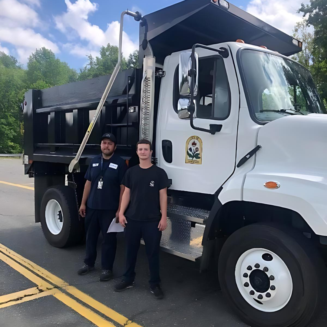 Two men are standing in front of a dump truck.
