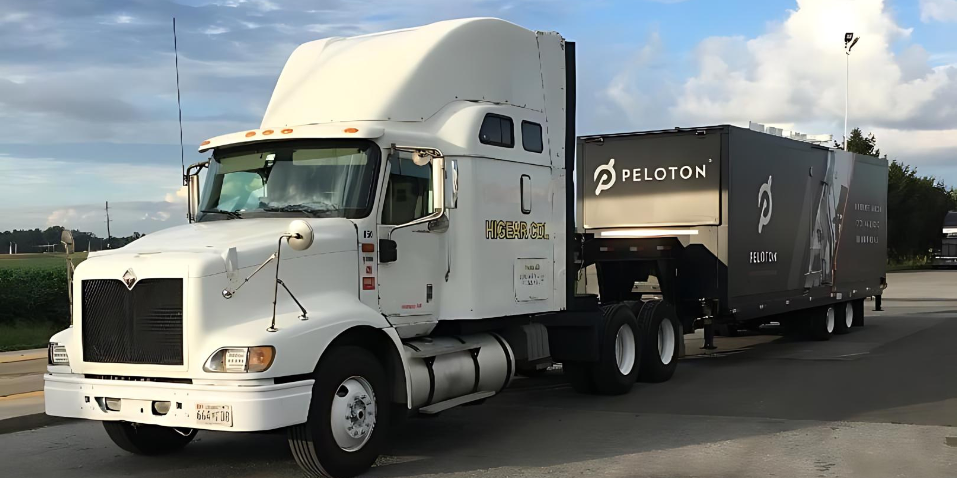 A white semi truck with a black trailer is parked in a parking lot.