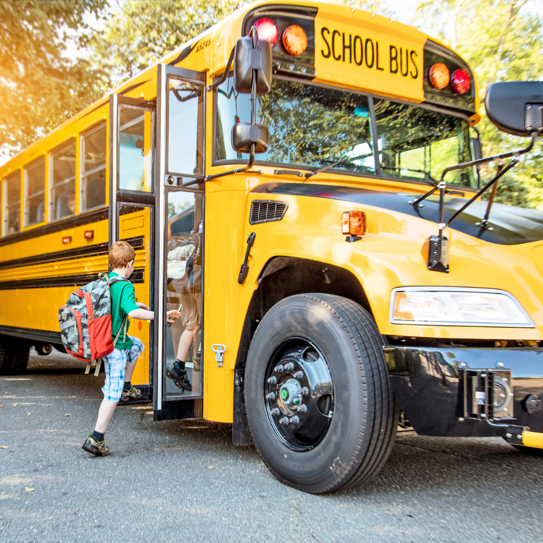 A boy is getting off a yellow school bus