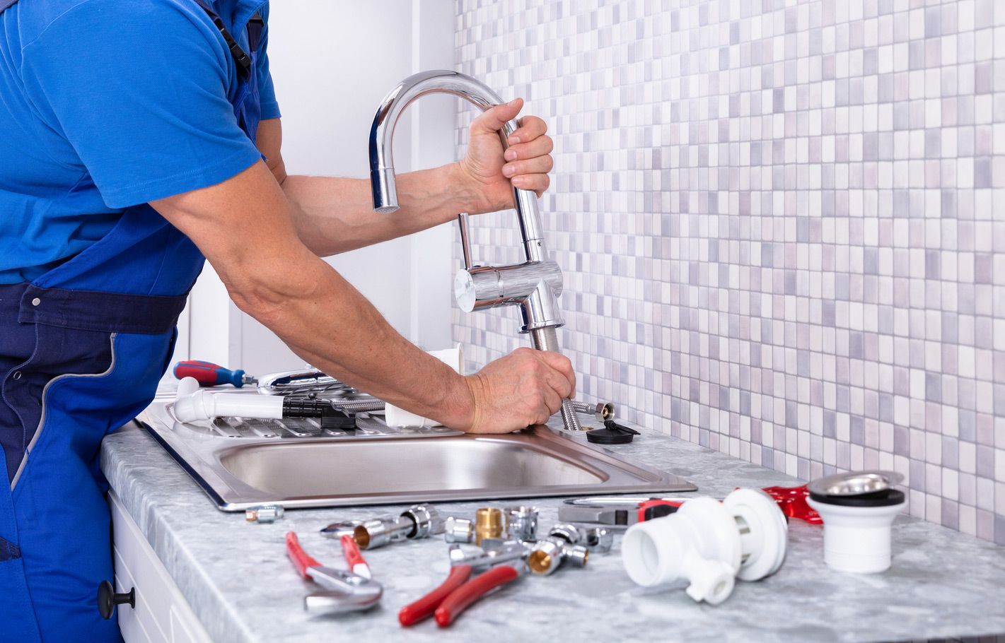 A plumber is fixing a sink faucet in a kitchen.
