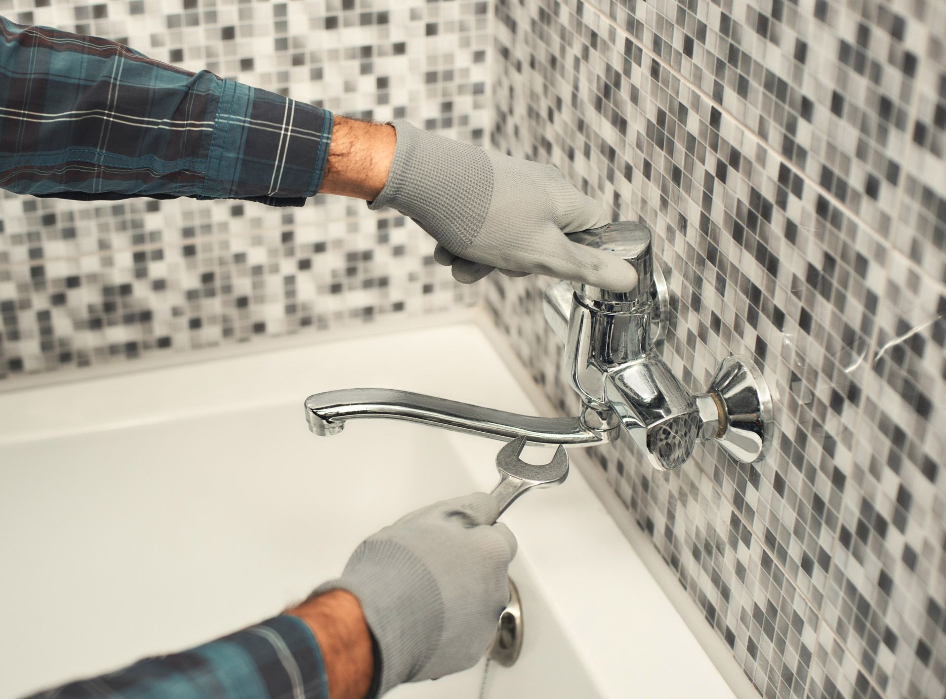 A man is fixing a faucet in a bathroom with a wrench.