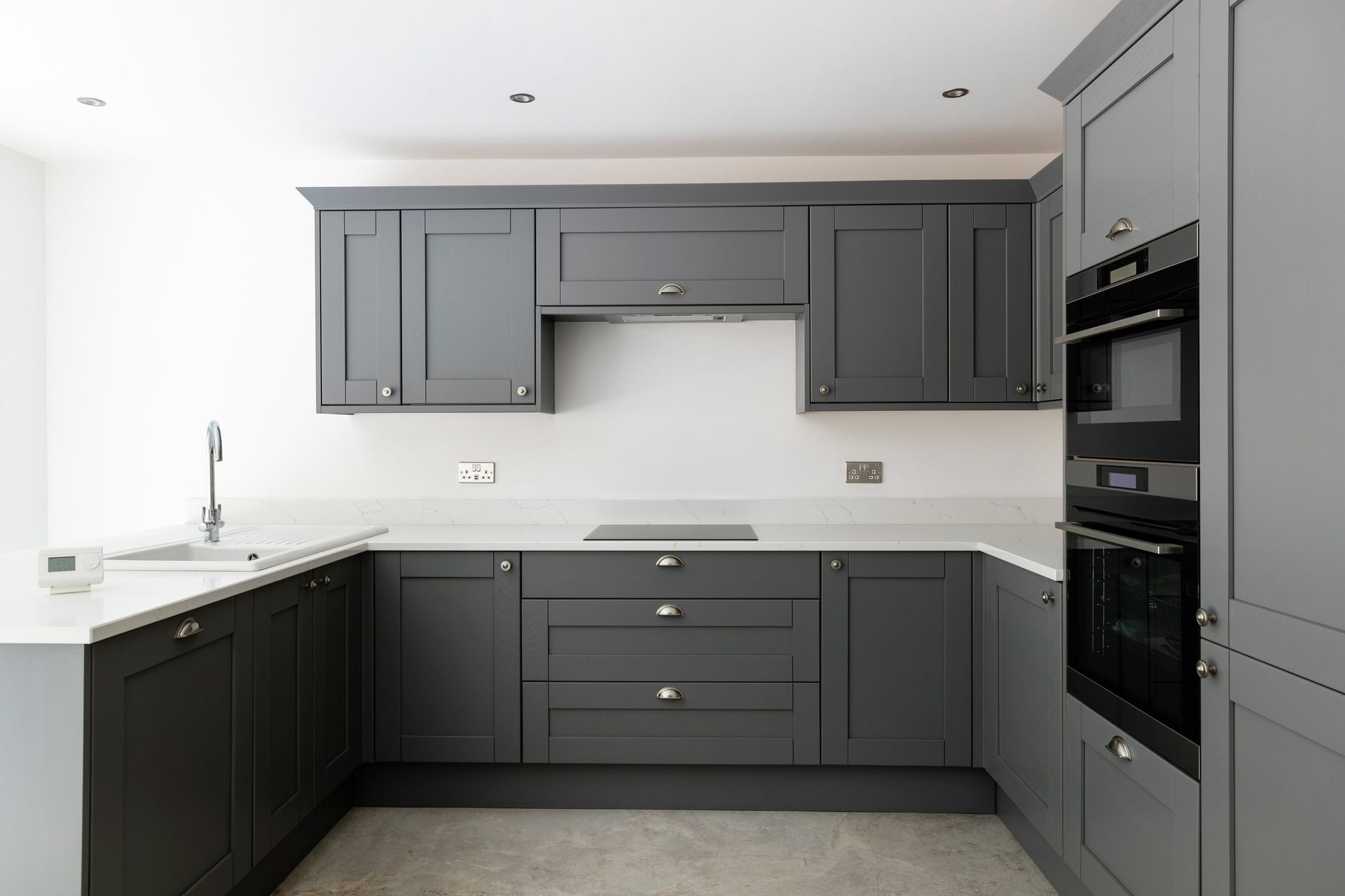 A kitchen with gray cabinets , white counter tops , and black appliances.