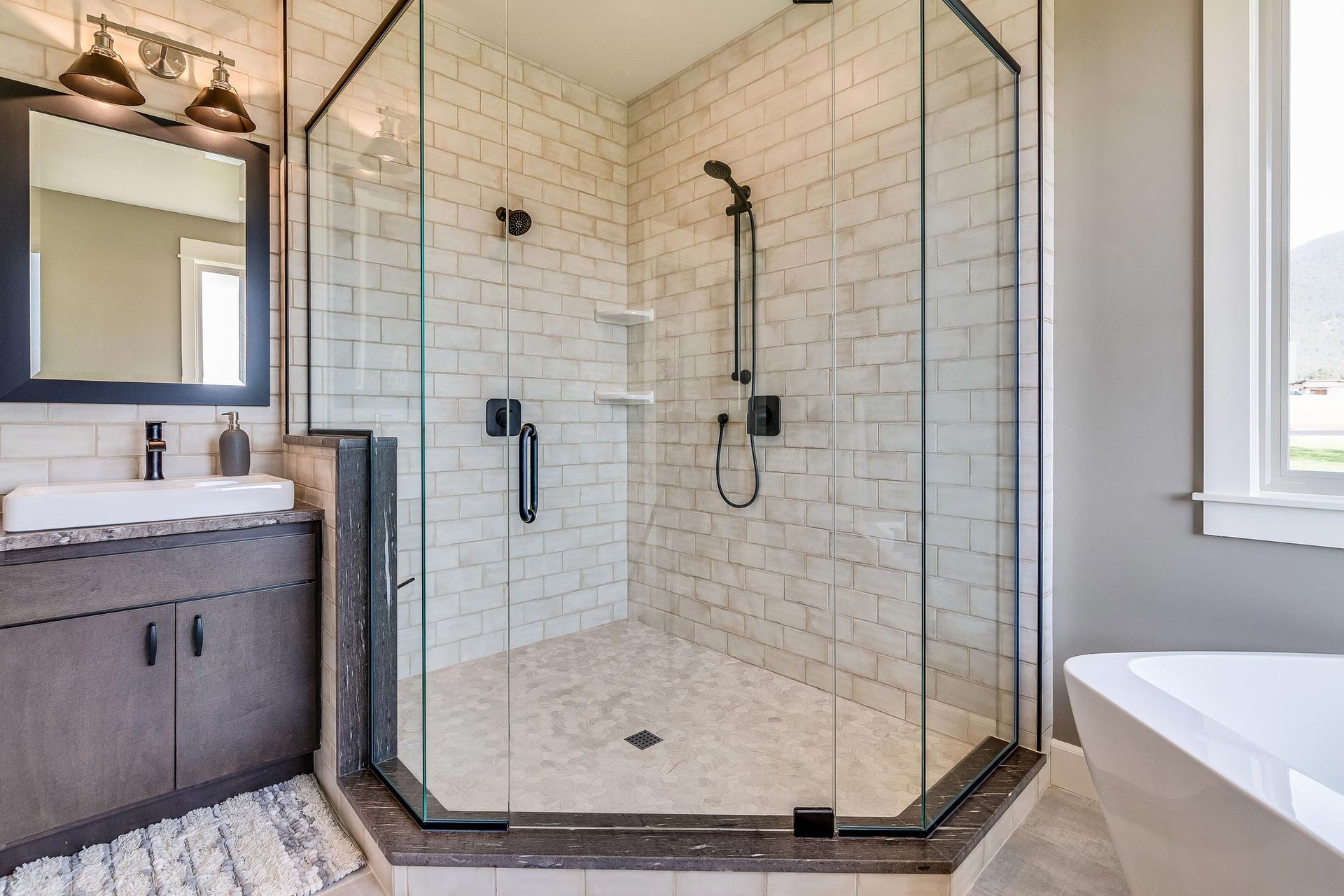A bathroom with a walk in shower , sink , mirror and tub.