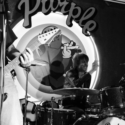 A man playing drums in front of a sign that says purple