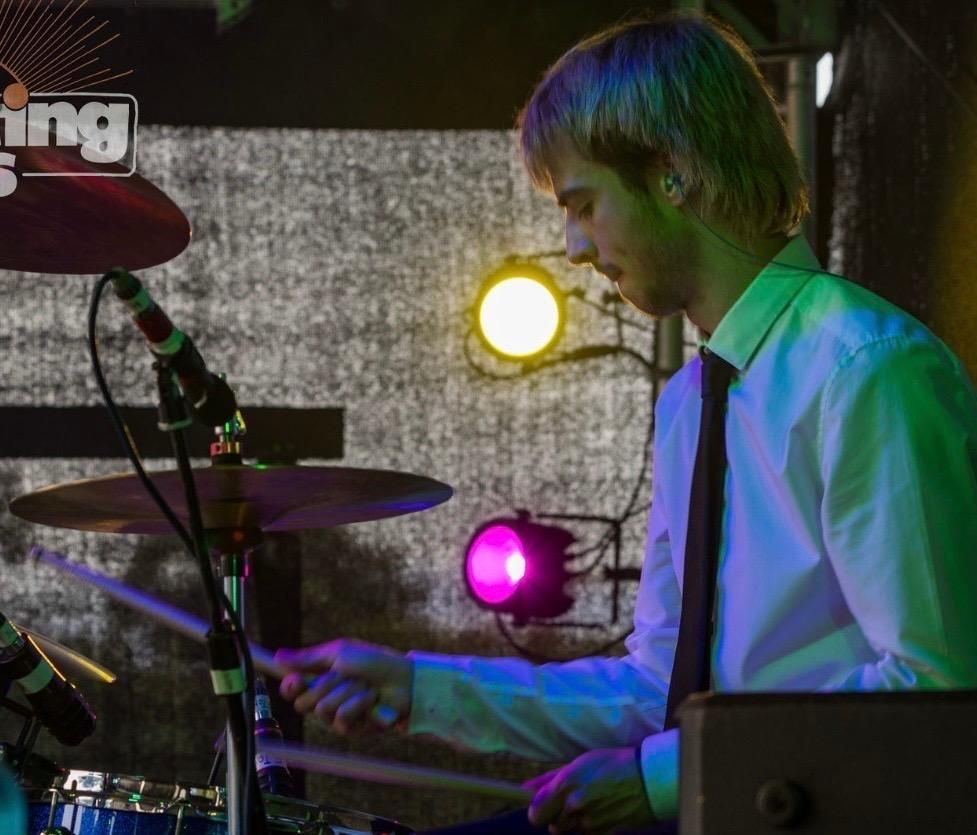 A man is playing drums in front of a sign that says king