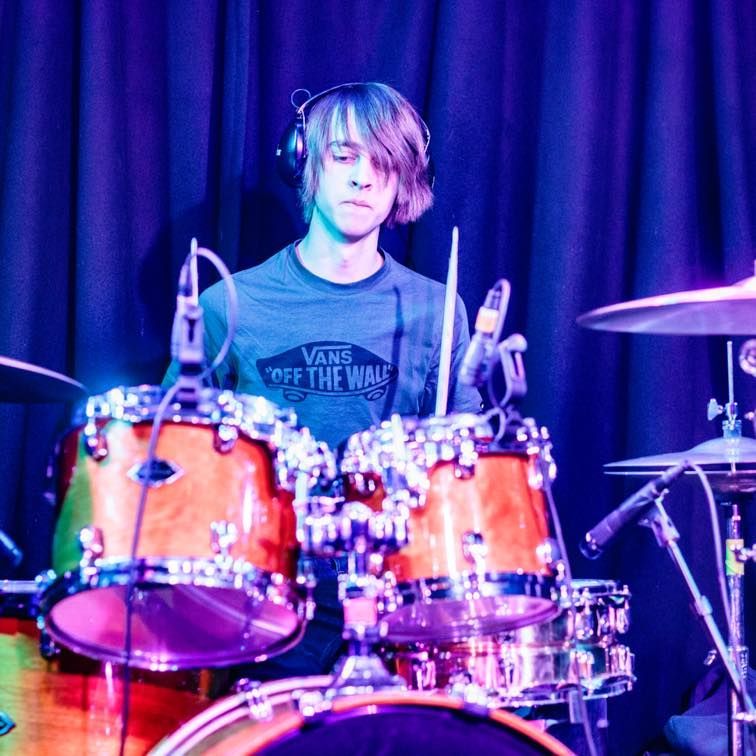 A man wearing a vans off the wall shirt is playing drums