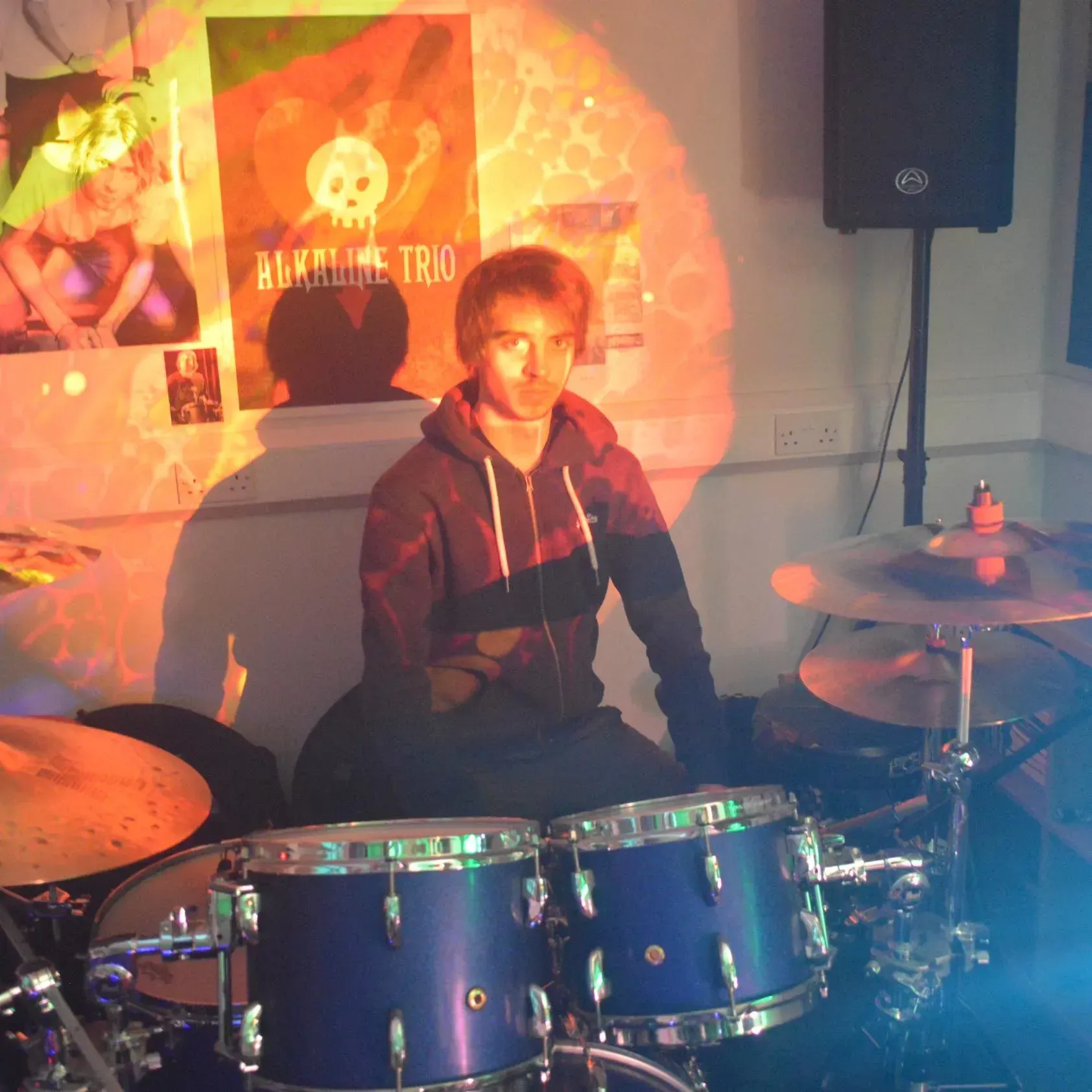 A man playing drums in front of a poster that says alkaline trio