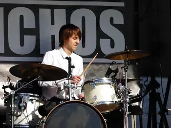 A man playing drums in front of a sign that says ichos