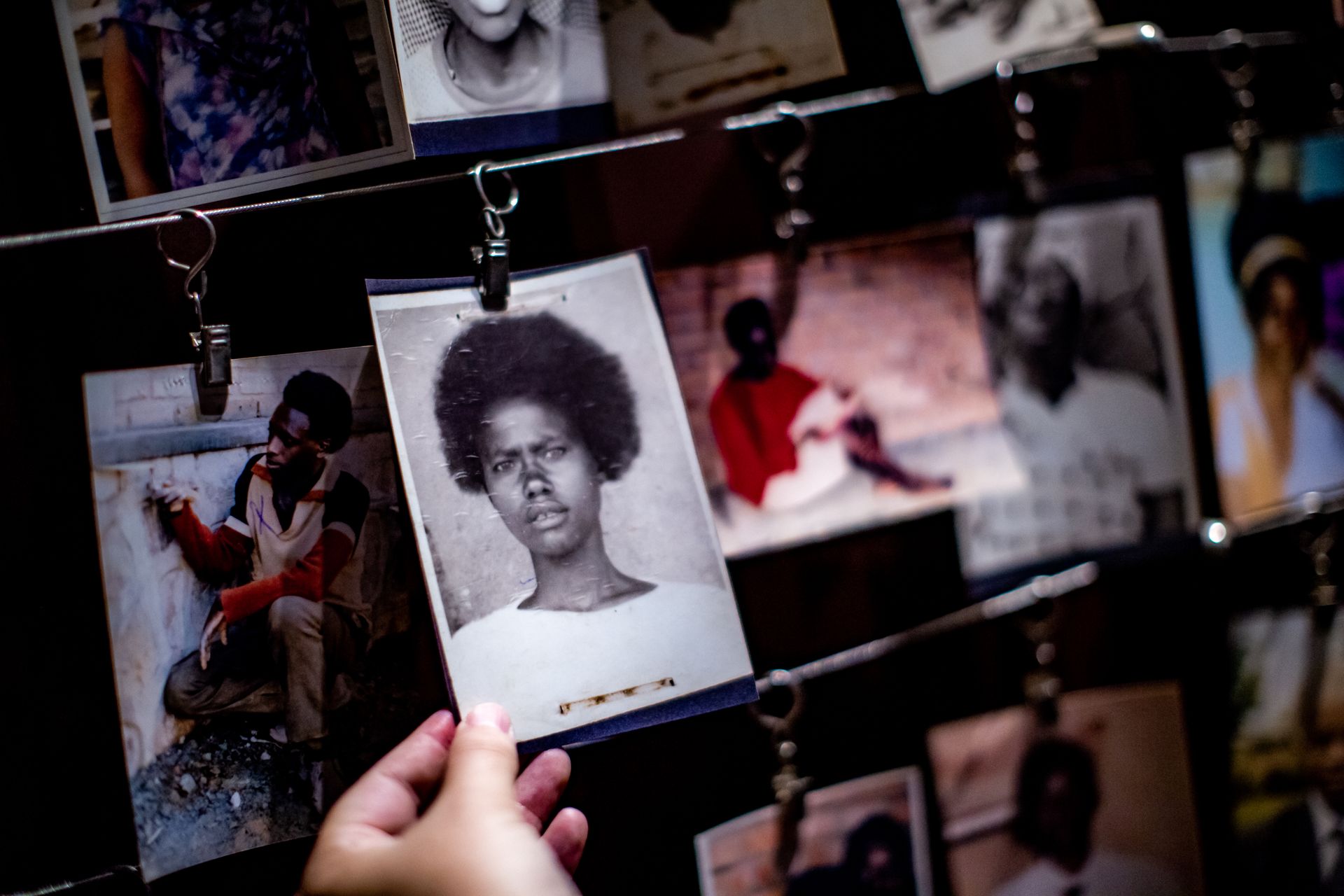 A hand holds a black-and-white portrait print hanging from a wire grid display filled with other photographs.