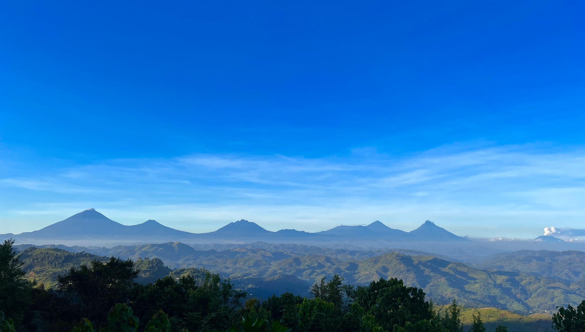 A green, cone-shaped mountain topped with layered, disc-shaped lenticular clouds against a blue sky.