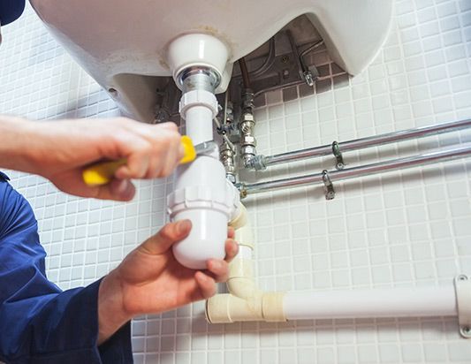 A plumber is fixing a sink pipe with a screwdriver.