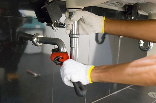 A plumber is fixing a sink pipe with a wrench.