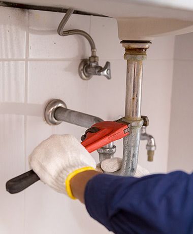 A plumber is fixing a sink with a wrench