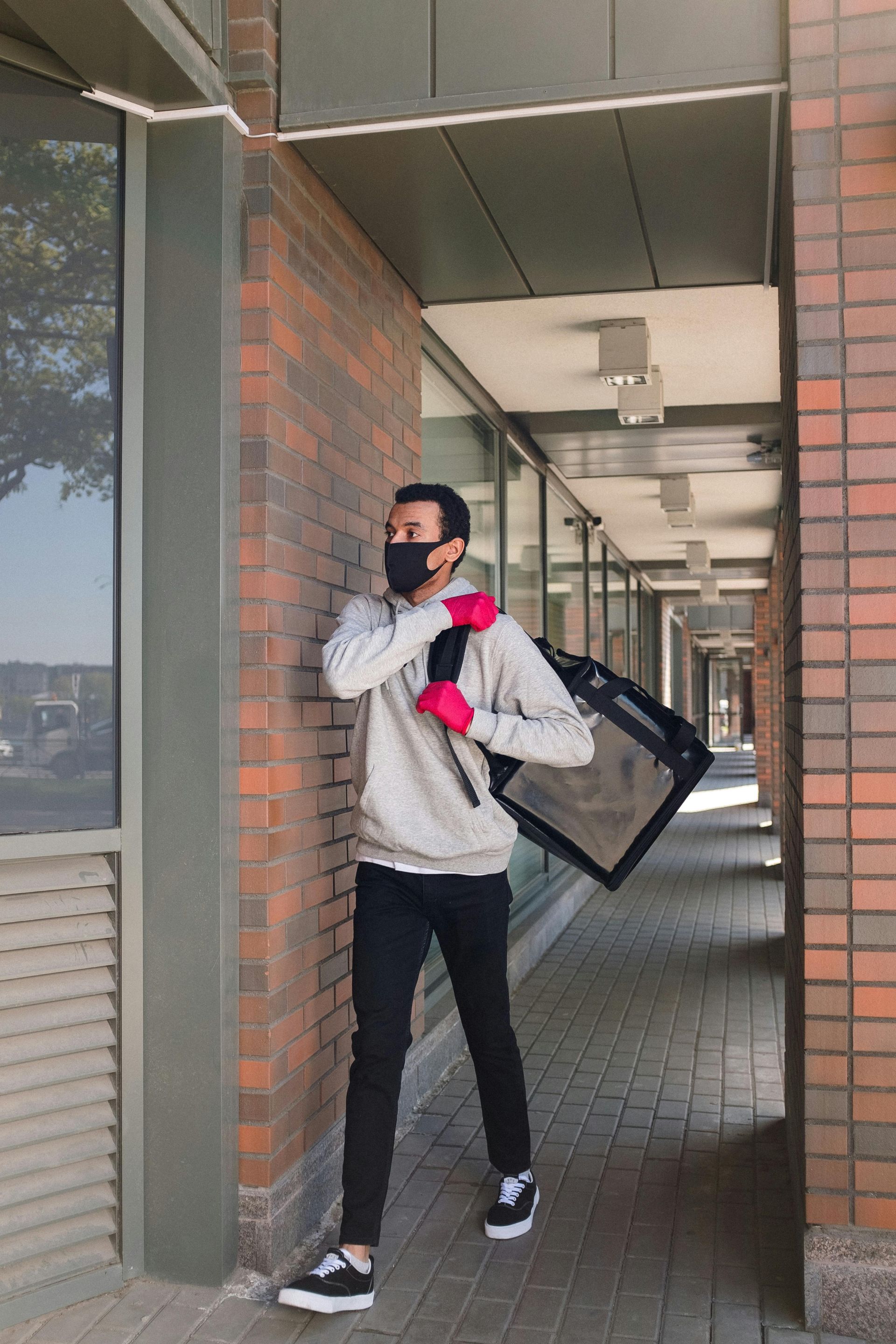 A man wearing a mask and gloves is carrying a bag.