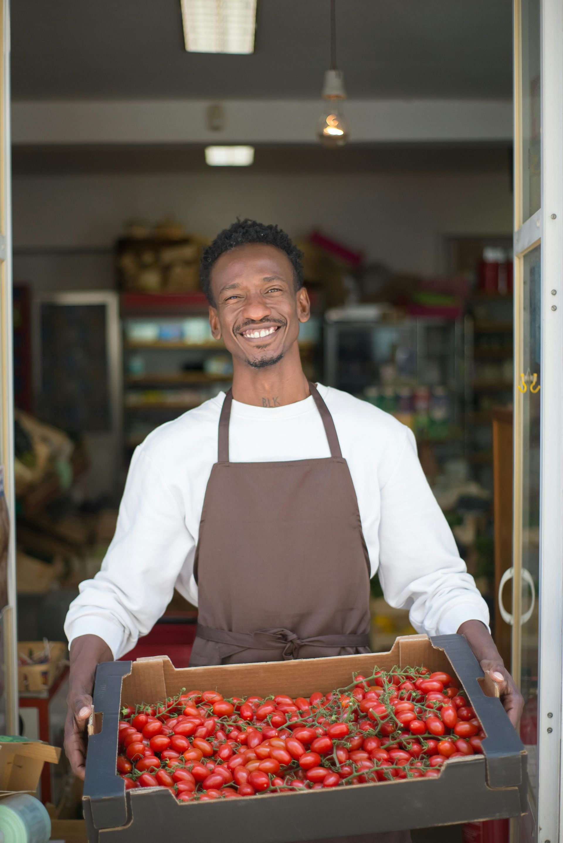 A man in an apron is holding a box of tomatoes.
