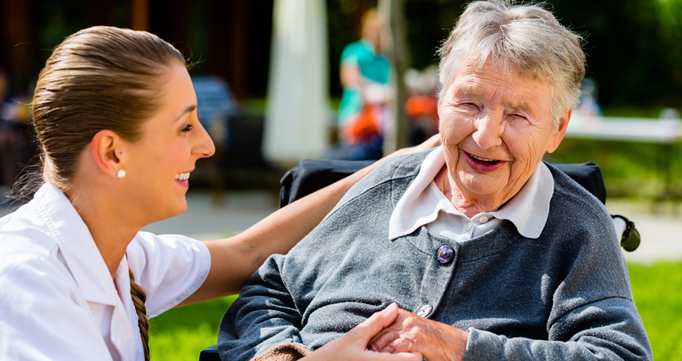 Female nurse talking and laughing with an elderly woman in a wheelchair