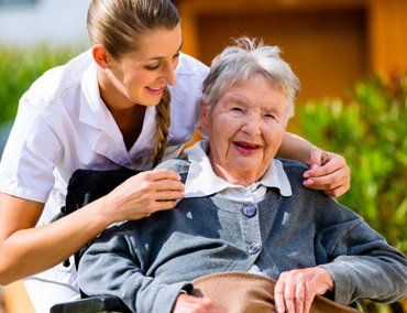 A female nurse holding an elderly woman sitting in a wheelchair by the shoulders