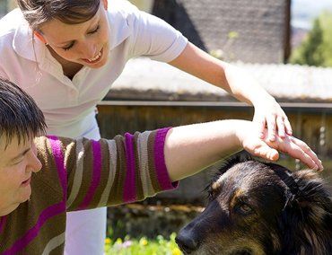 A female nurse and another person both petting a dog